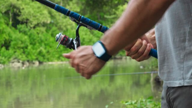 young guy with a fishing rod in his hands, twists a reel and fishes in a river in a rainforest.