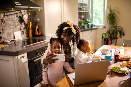 Single mother having breakfast with her two young daughters at home and having a selfie