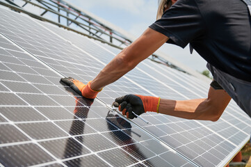 Close up of man hands in work gloves mounting photovoltaic solar panels. Male worker assembling solar modules for generating electricity through photovoltaic effect. Renewable energy sources concept.