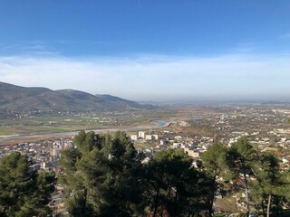 Sunny cityscape featuring a stunning view of a city from a hilltop, with a bright blue sky