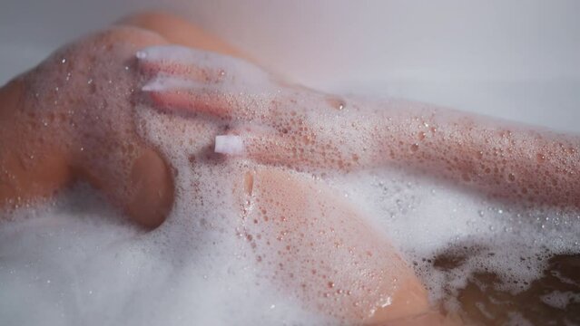 Woman applies foam on legs taking in bathtub