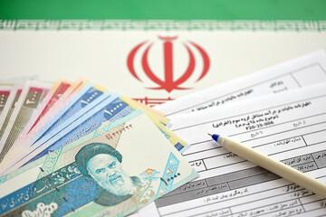 Iranian annual income tax return form F20-25-006 ready to fill on table with pen and iranian money on flag close up