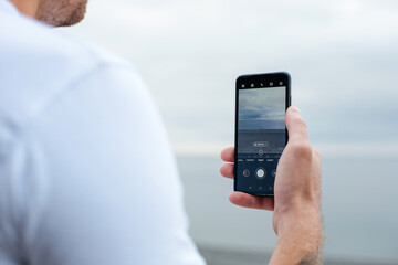 Close-up of a man's hand taking a picture of the sea and sandy beach on his phone