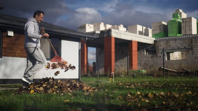 Caucasian man cleaning fallen leaves from lawn with broom in yard
