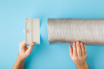 Man hands holding plastic adapter and corrugated aluminium pipe on blue table background. Point of view shot. Assembling new ventilation parts for kitchen cooker hood or air conditioning. Closeup. - obrazy, fototapety, plakaty