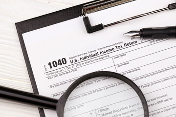 Form 1040 US Individual Income Tax Return on A4 tablet lies on office table with pen and magnifying glass close up