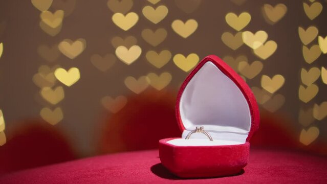 A gold engagement ring is in a jewelry box. Wedding ring as a symbol of renunciation and marriage. Marriage proposal concept. Red casket and diamond ring on light background