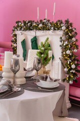 Table setting, silver wine glasses. Christmas tree in pink colors with a white decorative fireplace and candlesticks.