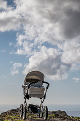 Fototapeta na wymiar An empty baby stroller is on top of a mountain with the sky with clouds in the background