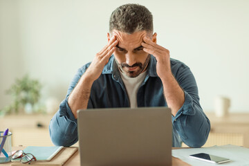 man having stress and headache while looking at laptop indoor