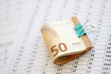 Heap of euro money bills in stationery clip on papers with calculations and receipts close up....