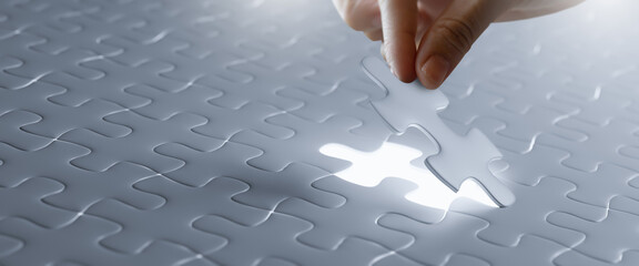 Hand put the last piece of white jigsaw puzzle to complete the mission.concept of...