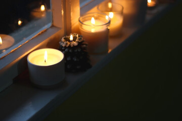 Lit candles and Christmas decorations on the window sill at night. Hygge at home. Selective focus.