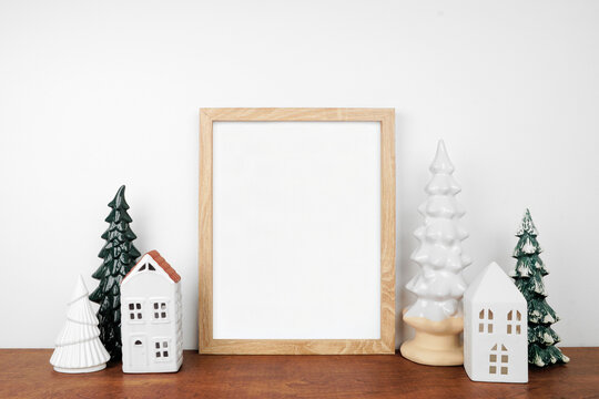 Christmas mock up with wooden frame, trees and white house decor. Portrait frame on a wood shelf against a white wall. Copy space.