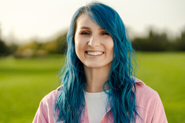 Smiling, beautiful young woman with blue hair looking at camera, standing on the street