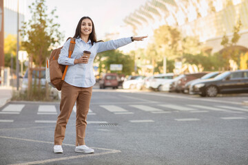 Cheerful pretty young caucasian woman tourist with backpack, cup of coffee takeaway, stop taxi