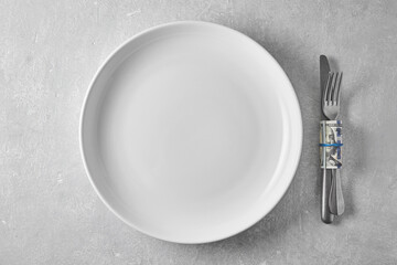 An empty white plate and a dinner fork and knife wrapped in a hundred dollar bill. Tips to the waiter in a restaurant