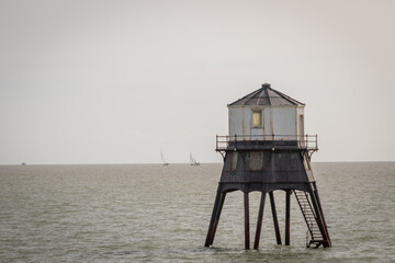 Fototapeta na wymiar Old lightouse in the sea, Dovercourt low lighthouse, built in 1863 and discontinued in 1917 and restored in 1980 the 8 meter lighthouse is still a iconic sight, with sailing boats sailing past