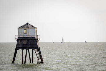 Old lightouse in the sea, Dovercourt low lighthouse, built in 1863 and discontinued in 1917 and restored in 1980 the 8 meter lighthouse is still a iconic sight, with sailing boats sailing past - obrazy, fototapety, plakaty