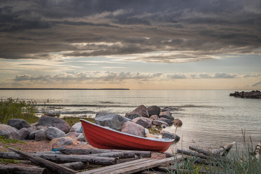 small boat on a beach, Image shows a small red dingy on a beach next to a wooden boat ramp with a number of smooth large rocks going out to a calm sea, during a summers sunset. August 2023