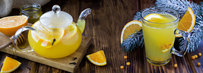 Hot tea with sea buckthorn and orange in the glass cup and teapot on the rustic wooden background....