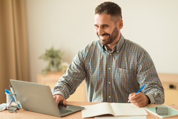 Man Working Online Taking Notes Near Laptop, Sitting At Office