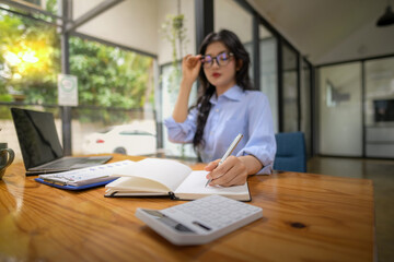 Close-up of a woman holding a pen to write something in a notebook.