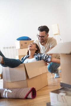 Happy overjoyed young couple first time home buyers owners having fun unpacking riding in box on moving day.