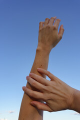 Examining Freckled Arms in the Sky. A hand carefully examines freckled arms against a clear blue sky, highlighting the beauty of ephelides