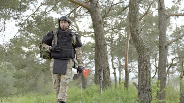 Demining. Soldier with a backpack walks near the trees. Neutralizing mines