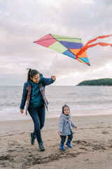 Little girl walks next to her mother with a colorful kite in her hand