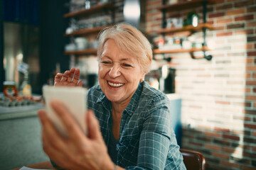 Smiling senior woman talking on smartphone video call at home