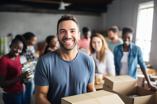 Portrait of male volunteer with charity box and international group of people at distribution center.