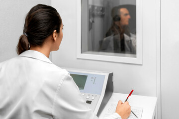 Audiologist woman doing the hearing exam to a mixed race manwoman patient using an audiometer in a special audio room.