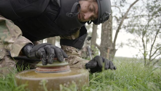 Military sapper demining an anti-tank mine in the field near the forest. Ukrainian Explosive Ordnance Disposal Officer detecting metal by metal detector device