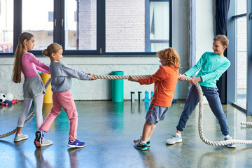 preadolescent children in sportswear playing tug of war with fitness rope in gym, child sport