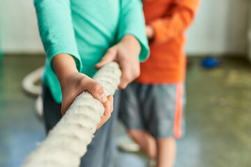 cropped view of two children in sportswear pulling fitness rope in gym, child sport