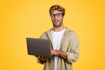 Surprised European man with laptop, looking at camera, yellow background