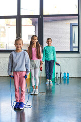 vertical shot of pretty little girls and boy with jump ropes in hands smiling at camera, child sport