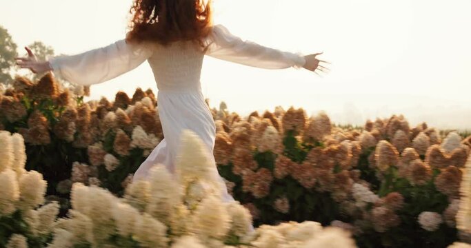 Beautiful red-haired woman in white elegant dress running on blooming field.