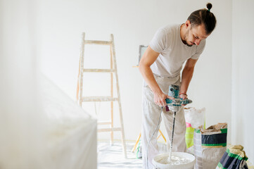 A worker is mixing plaster with manual mixer in a house and renovating.