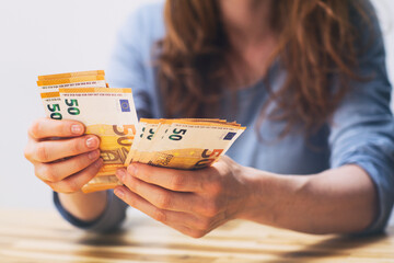 Caucasian woman with red hair counting Euro banknotes at a table at home