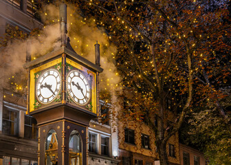 Fototapeta na wymiar Iconic Gastown Steam Clock illuminated at night on Water Street with fall foliage trees and lights in the background on a beautiful autumn evening, Vancouver, British Columbia, Canada (October 2021).