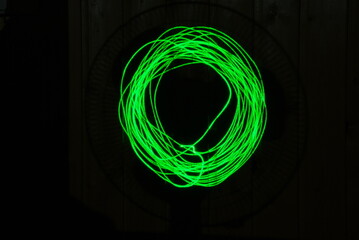 Image of a circle on a black background. A hand-drawn circle on a dark surface. It is made using a green laser with multiple repetitions of a geometric figure.