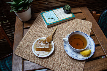 Morning setup on wooden table at balcony, books to read, cup of natural tea, teapot, organic honey...