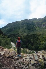 Fototapeta premium A woman looks at the Dolra river, a hiker, walks along a stony path. travel concept. Trail to Shdugra Waterfall. Caucasus Mountain Range in Georgia, Svaneti Region. Wanderlust. Vertical photo