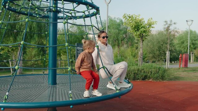 Young happy mother and baby on a carousel in a playground. High quality 4k footage