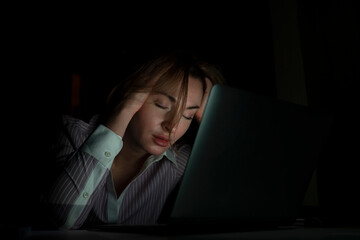 Side view of young tired businesswoman working on laptop at night. Work from home concept