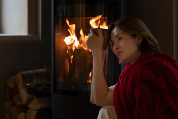 Young attractive woman sitting close to fireplace, reading interesting book and drinking hot tea in the cozy house