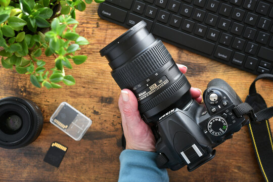 Photographer holding DSLR Nikon camera with zoom lens at desk with SD cards and computer keyboard